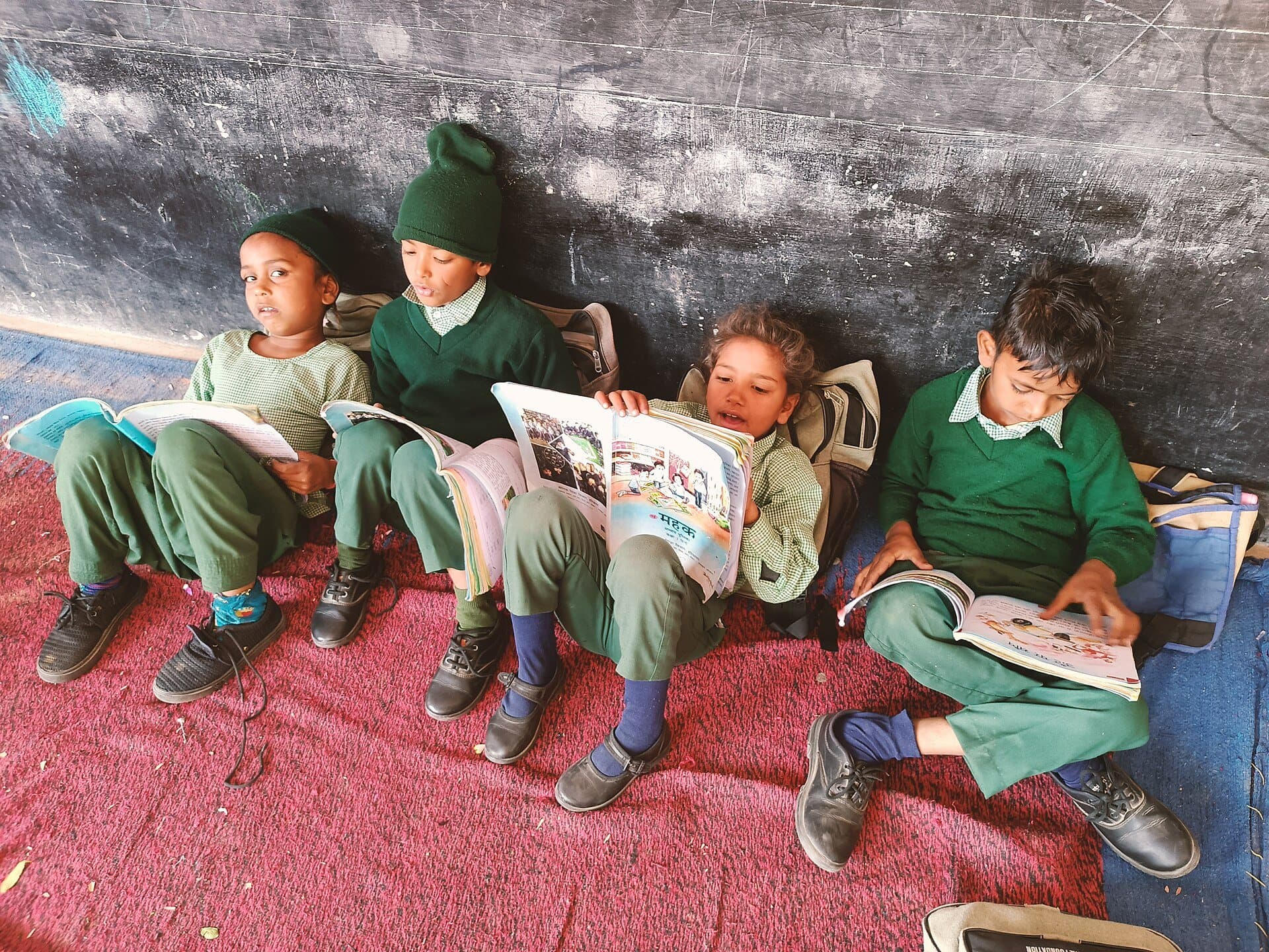 Schoolchildren in uniform reading books against a blackboard