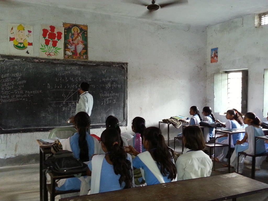 A teacher at the blackboard in front of a full classroom