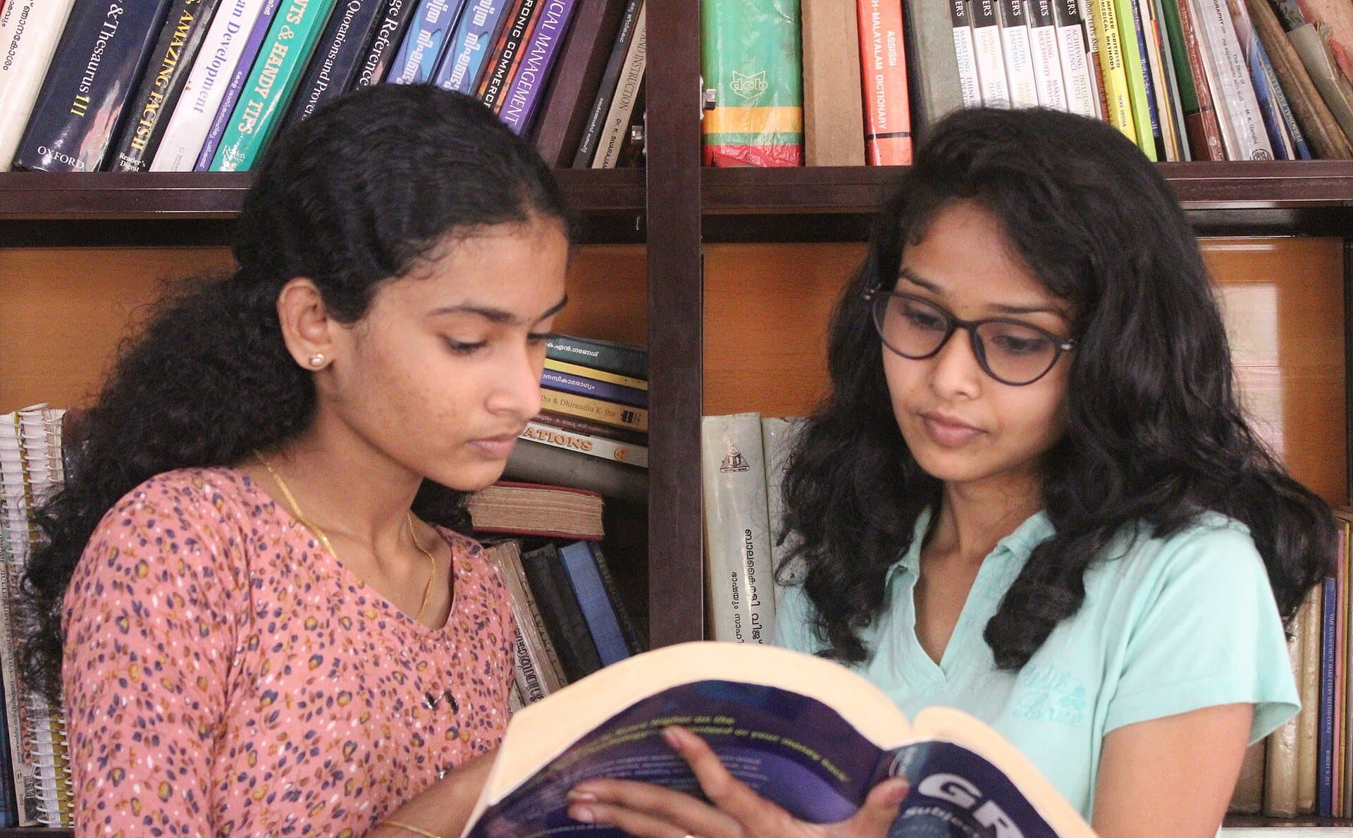 Two students reading a book together in a library