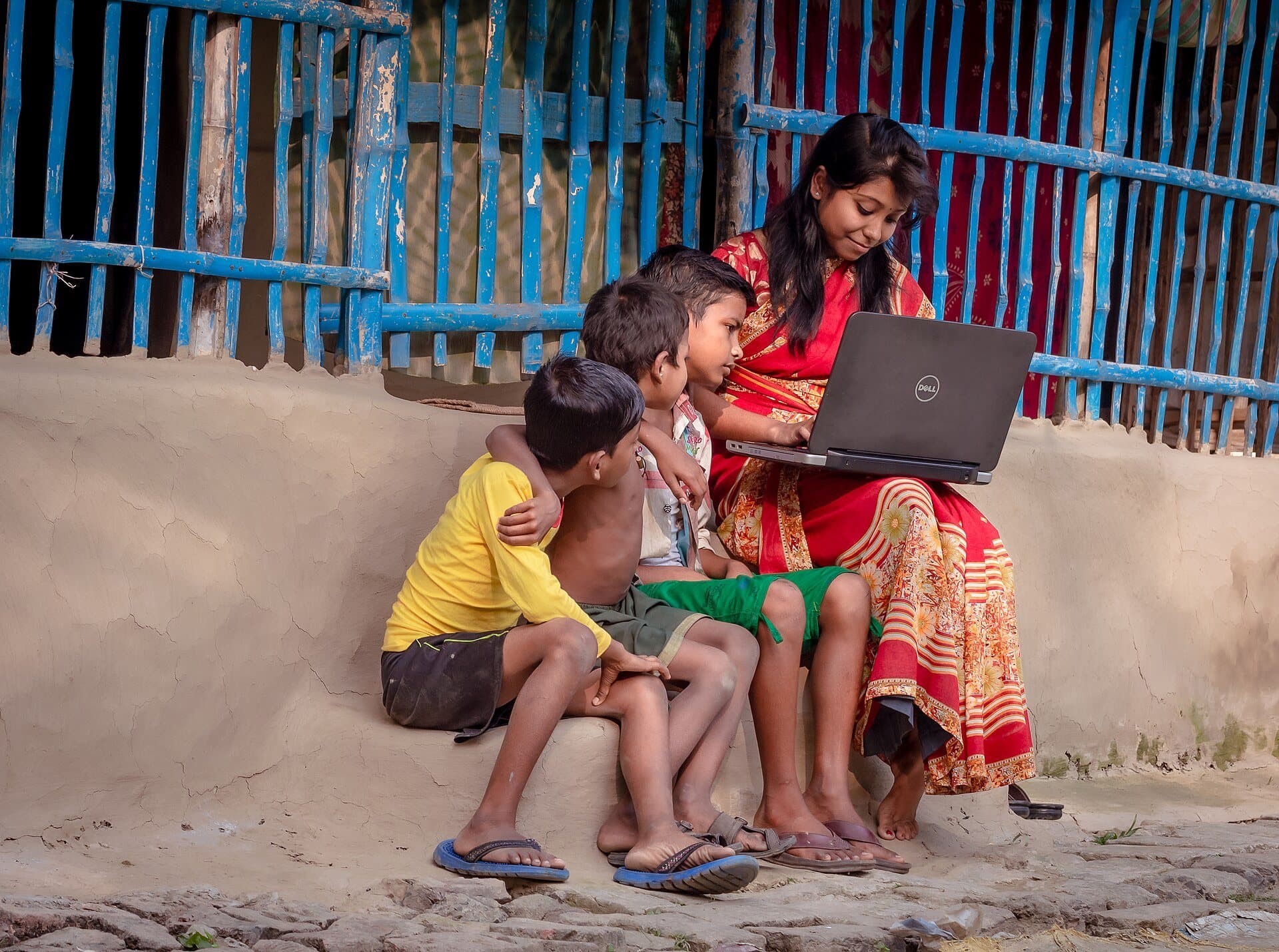 A volunteer teaching children on a laptop outside a village home